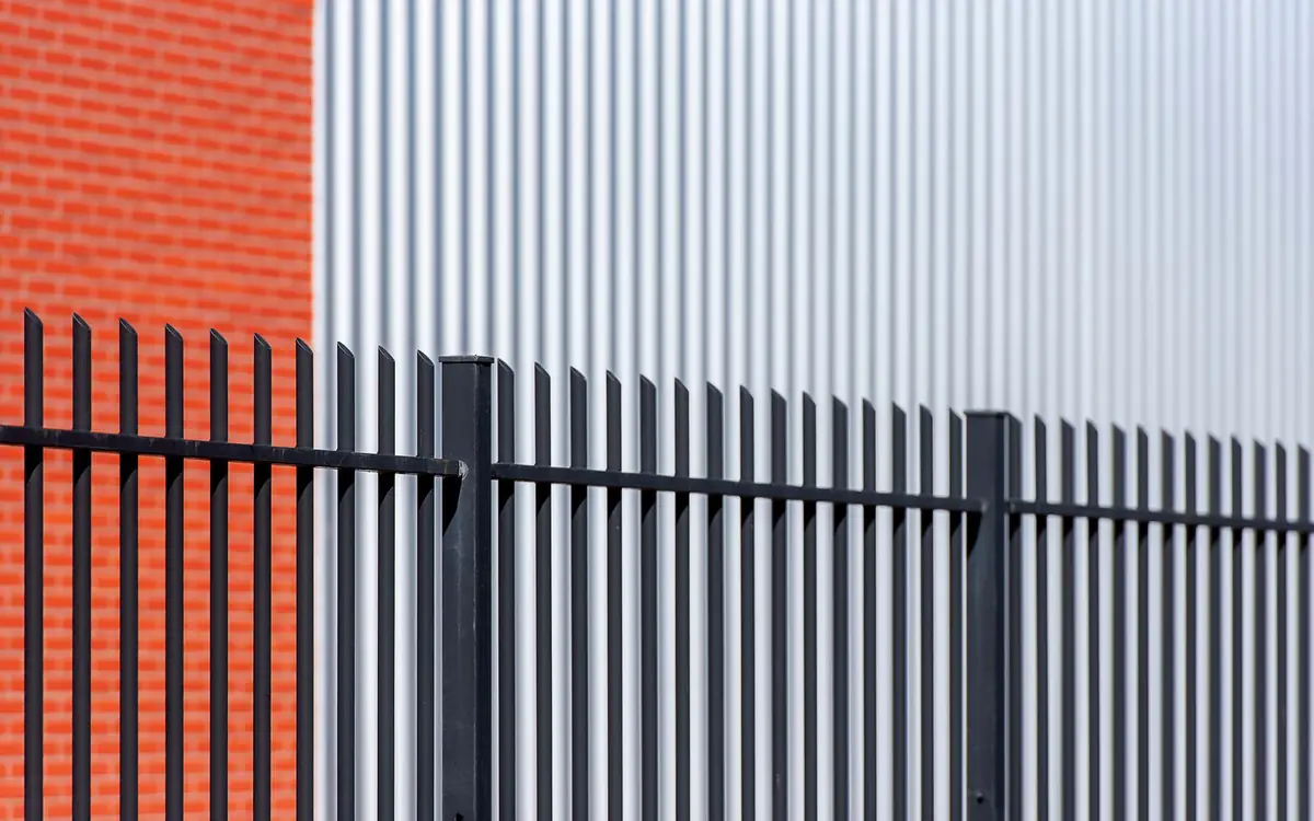 Black steel picket security fence along a commercial building with brick and metal siding