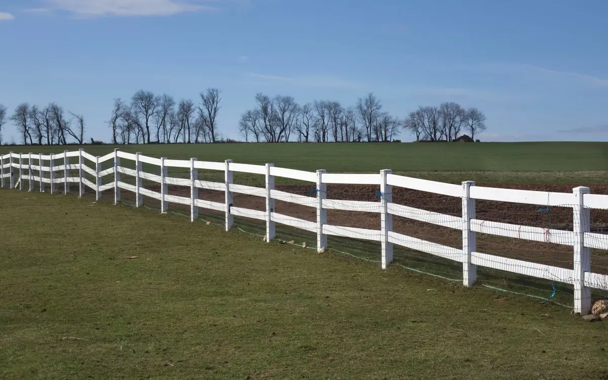 Long white three-rail board fence along a grassy field under blue sky