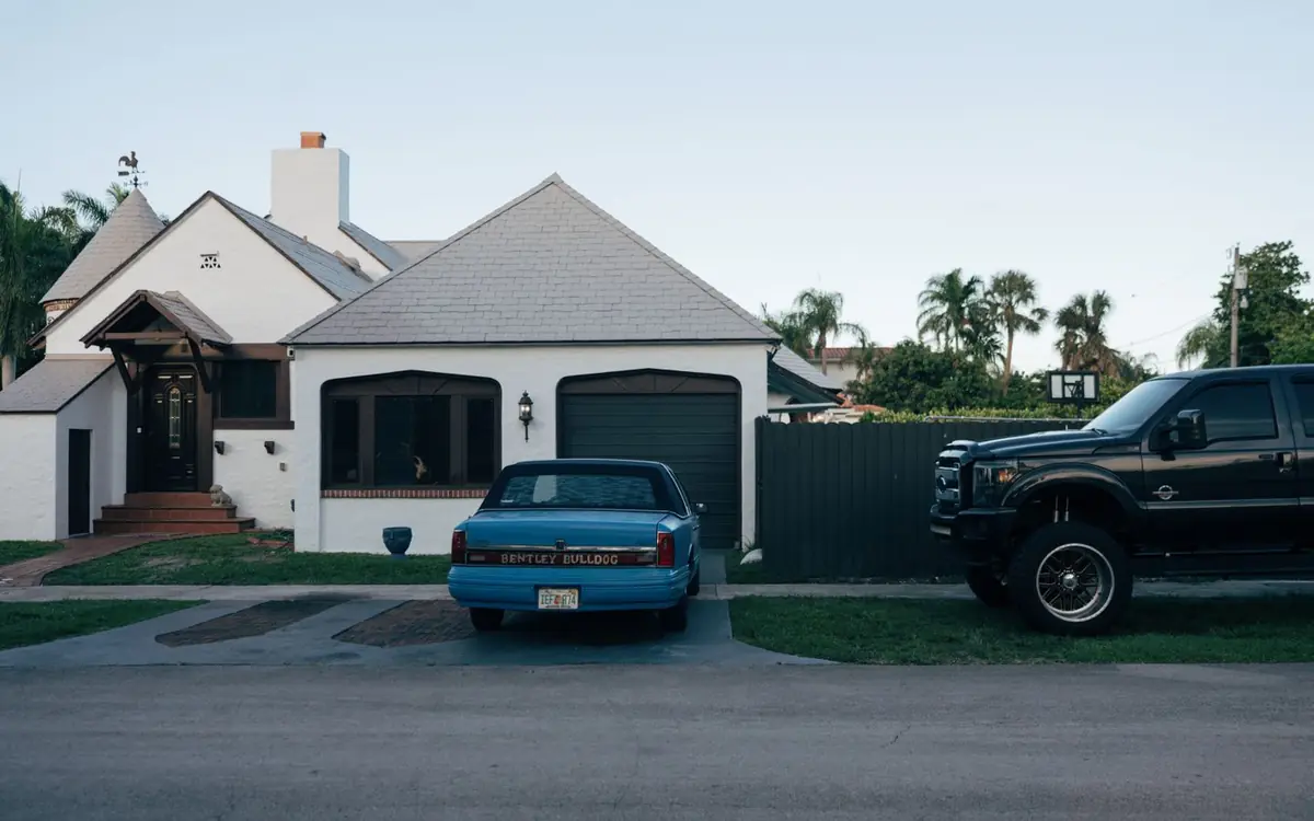 White Florida home with a black privacy fence beside the driveway and palm trees