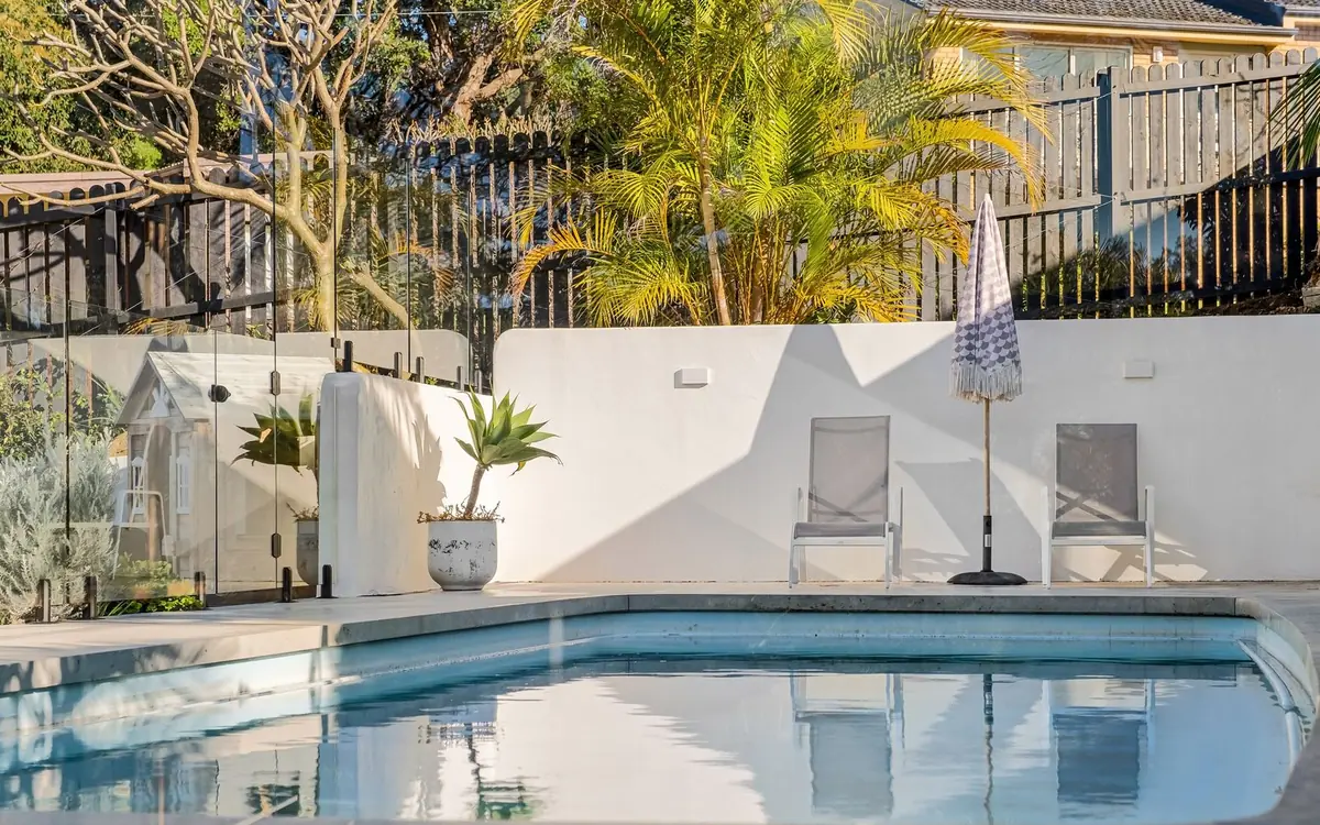 Backyard pool with white walls and a black metal pool fence among palm trees