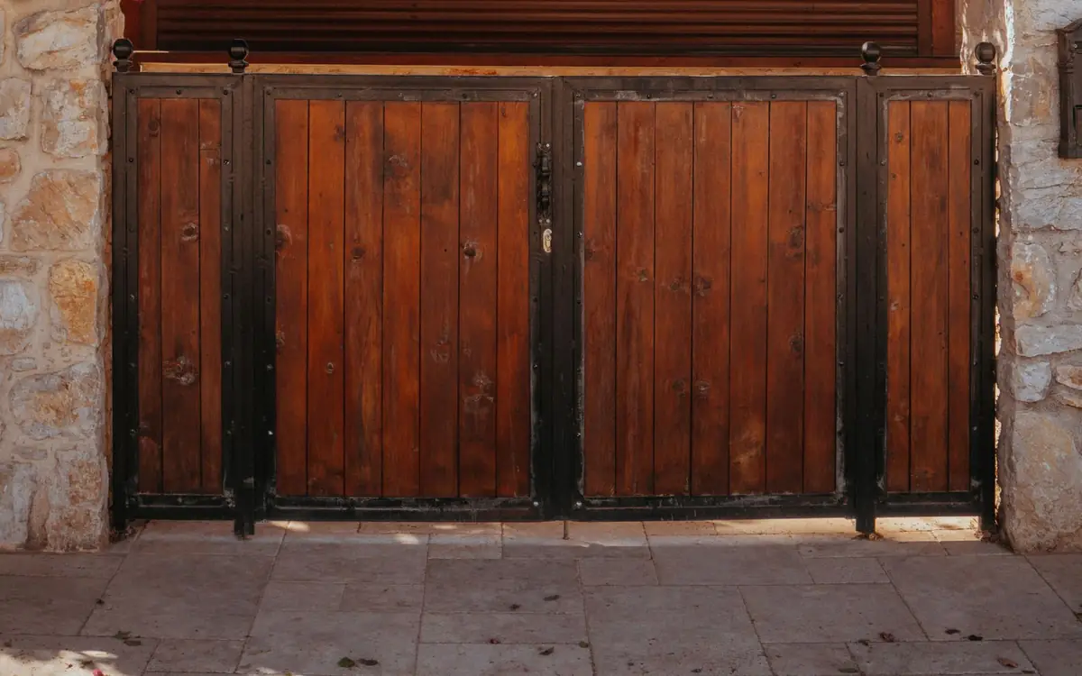 Double wood driveway gate in a black steel frame between stone columns