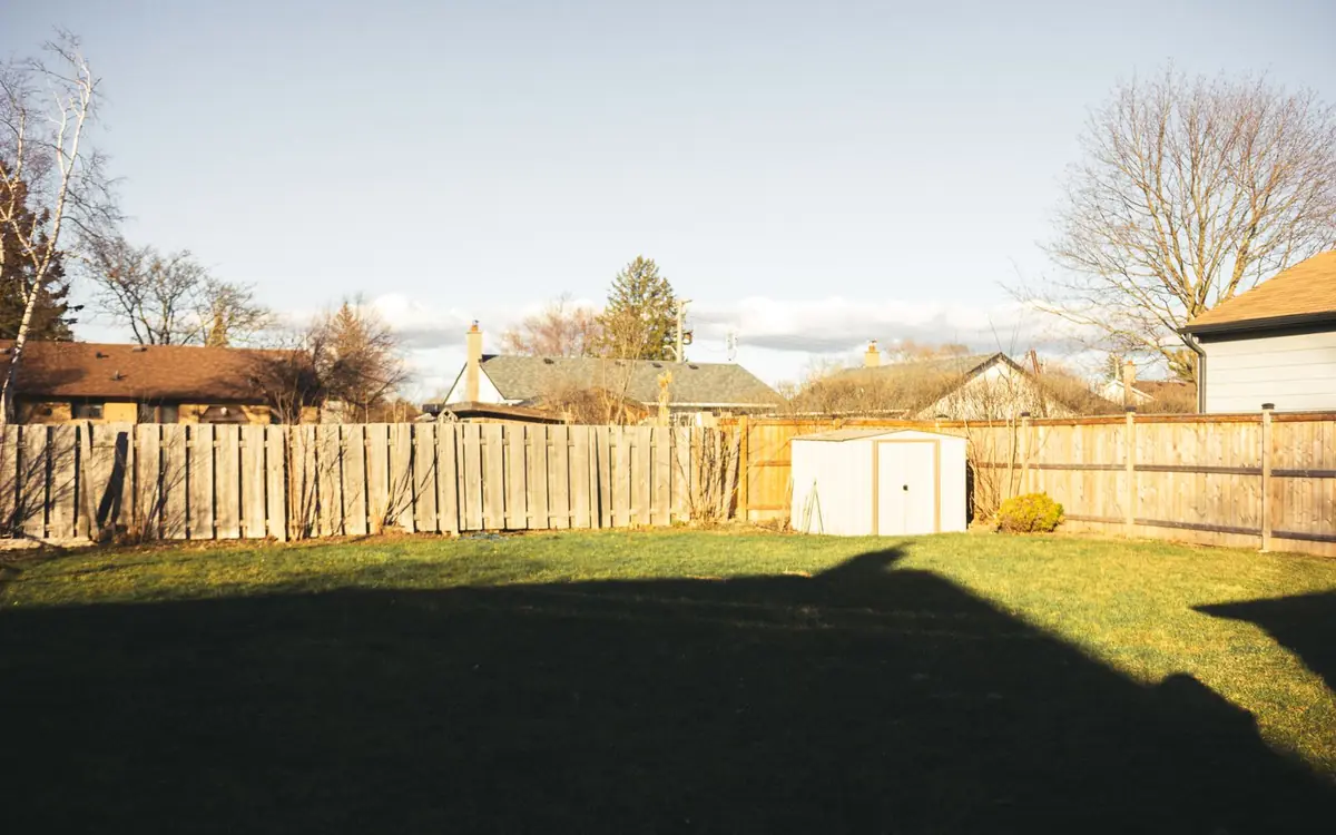 Back yard enclosed by a wood privacy fence with a storage shed and green lawn