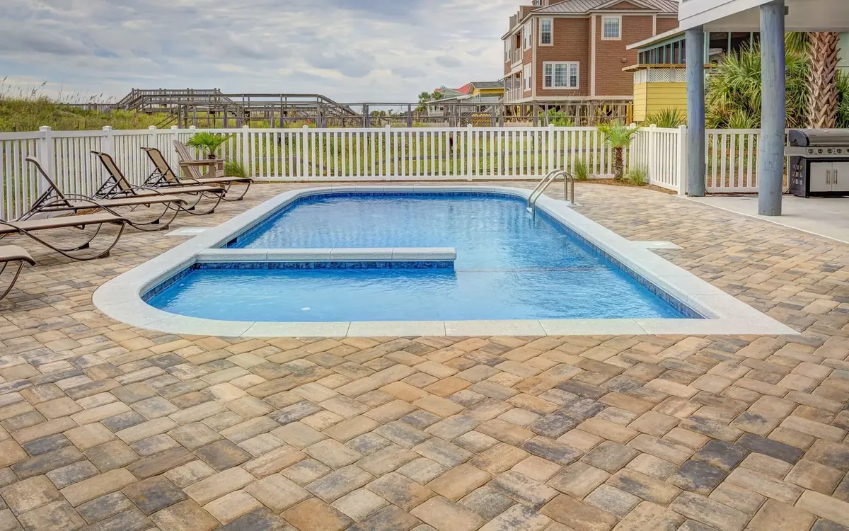 In-ground pool with paver deck surrounded by a white fence