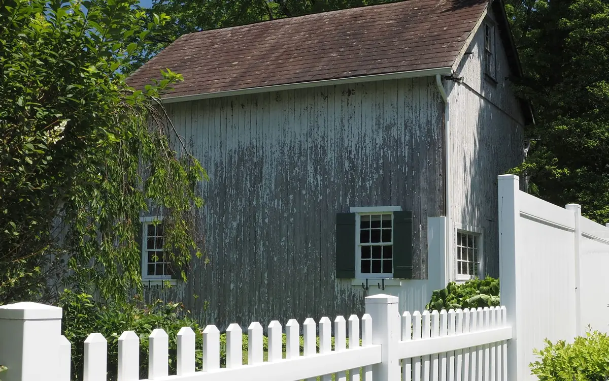 White vinyl picket fence in front of a gray farmhouse with a vinyl privacy section behind