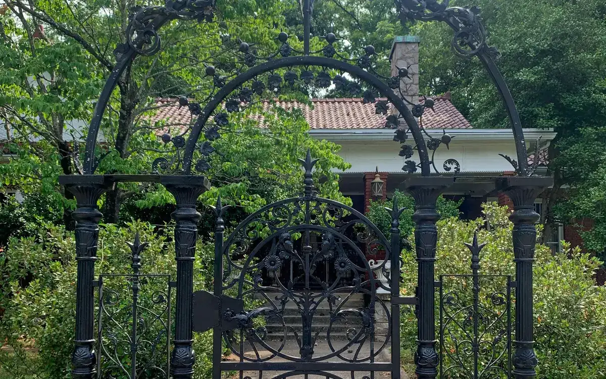 Ornate black wrought iron arched entrance gate with columns in a garden